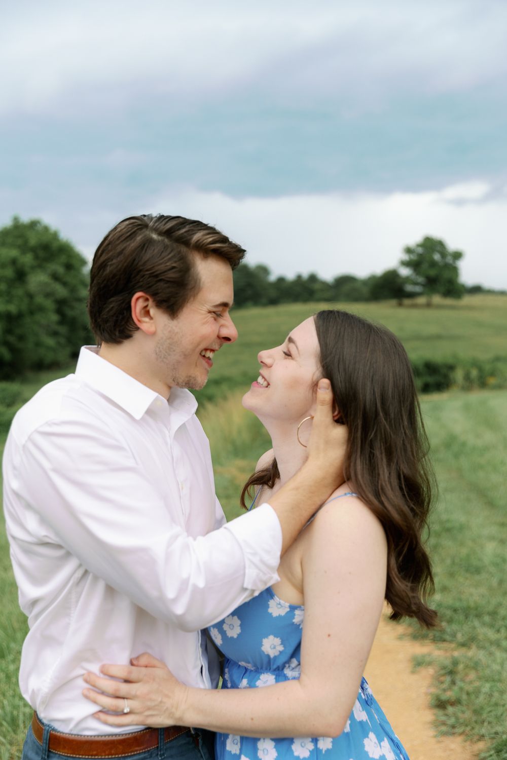 A romantic couple laughing together in a grassy field on a cloudy day.