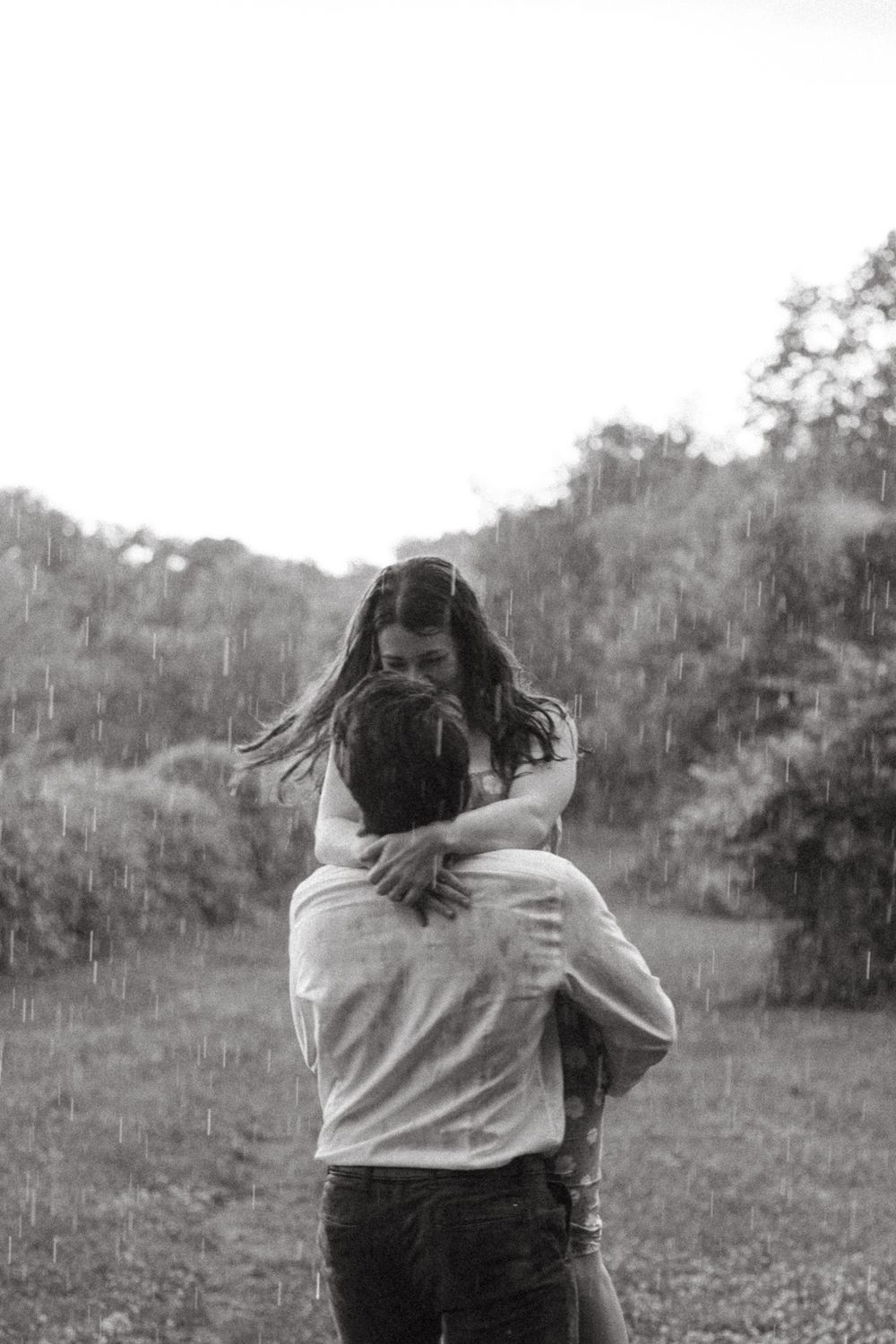 A couple sharing a playful embrace in a field on an overcast day.