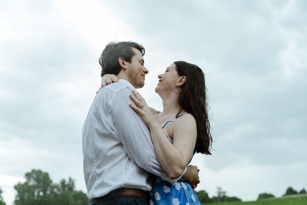 Romantic couple sharing tender moments in a green field under cloudy skies.