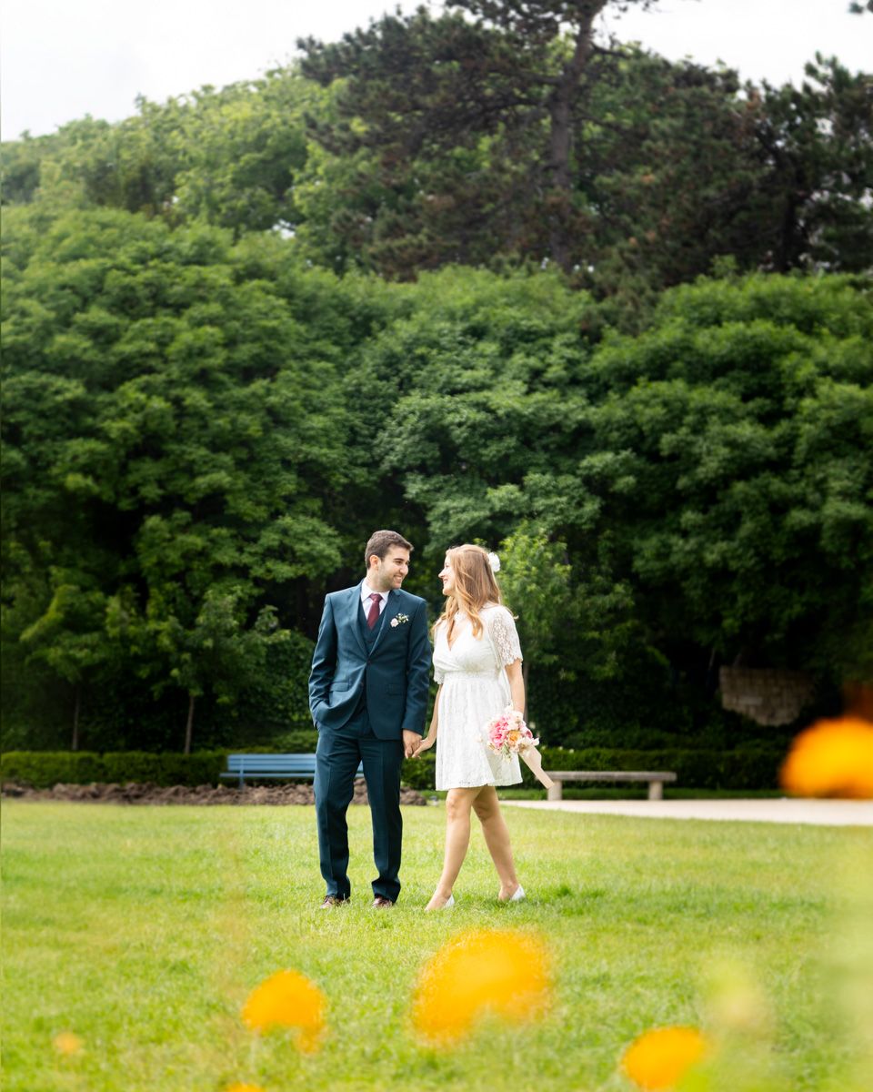 A couple walking through a lush green park with yellow flowers in the foreground.