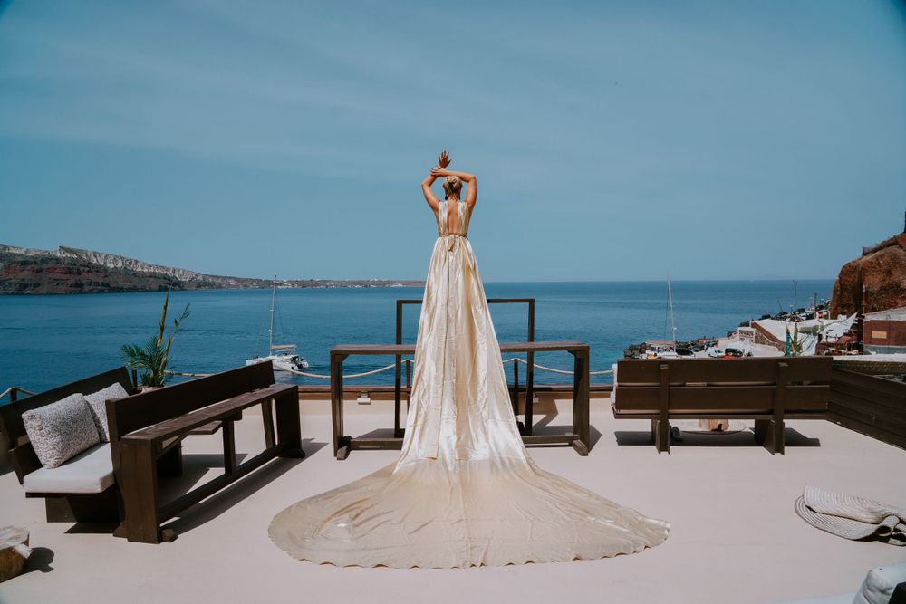 An elegant bridal gown with long train photographed on a Santorini terrace with ocean views.