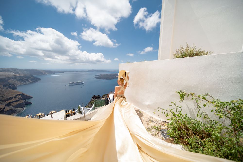 Long golden dress train sweeping down white steps with Mediterranean Sea views.