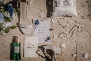 Wedding stationery and details flat lay with blue flowers and pearls on textured surface.