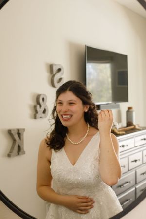 A bride wearing pearls and lace dress laughs joyfully in an indoor setting.