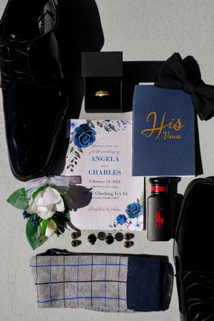 Wedding details including navy blue invitations, shoes, and floral accents arranged on a gray surface.