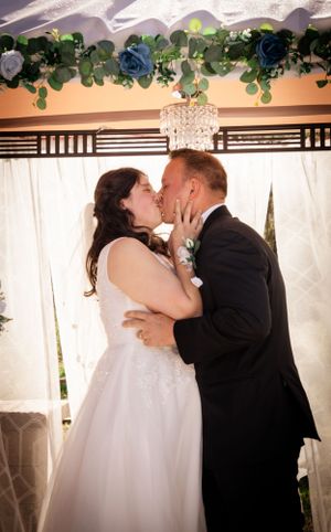 Wedding ceremony kiss sequence under decorated archway with white curtains and greenery.