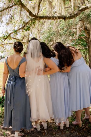 Wedding party in blue and white dresses standing together under moss-covered trees.