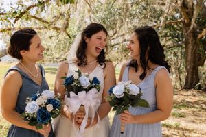 Bridesmaids in light blue dresses share joyful moments outdoors.