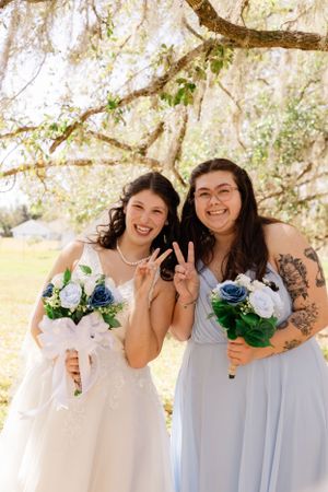 Bridal party in blue dresses poses playfully with bouquets under Spanish moss trees.