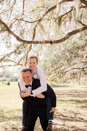 Playful groomsmen pose for candid photos under Spanish moss draped trees in a natural outdoor setting.