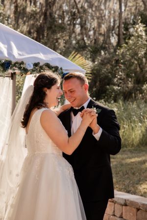Couple shares romantic first dance moment under draped outdoor wedding arch.