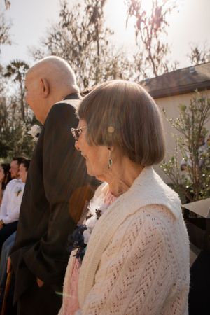 Wedding guests watch the ceremony from outdoor seating on a sunny day.