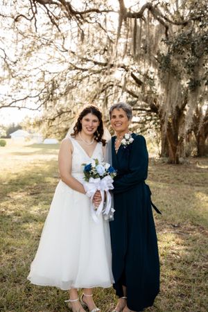 Two children in formal attire pose together under moss-draped trees.