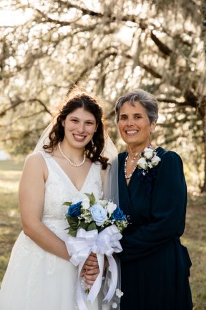 Bride in white dress poses with family member wearing navy at outdoor wedding.