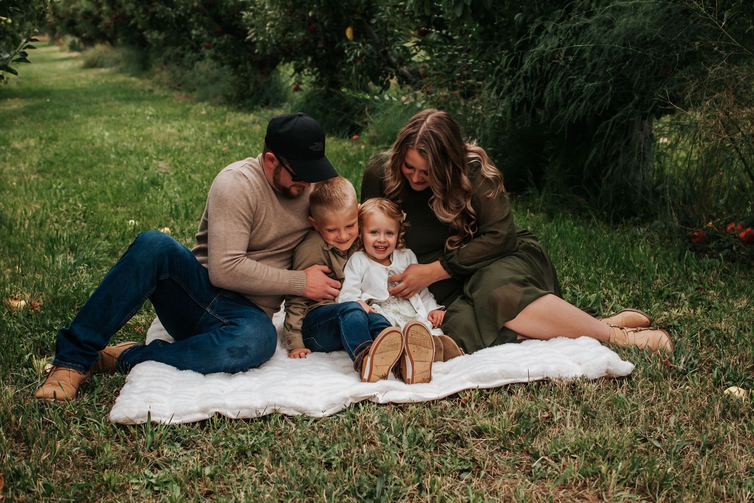 A family sits together on a white blanket in Kendall Farms apple orchard, Benton City, Washington.
