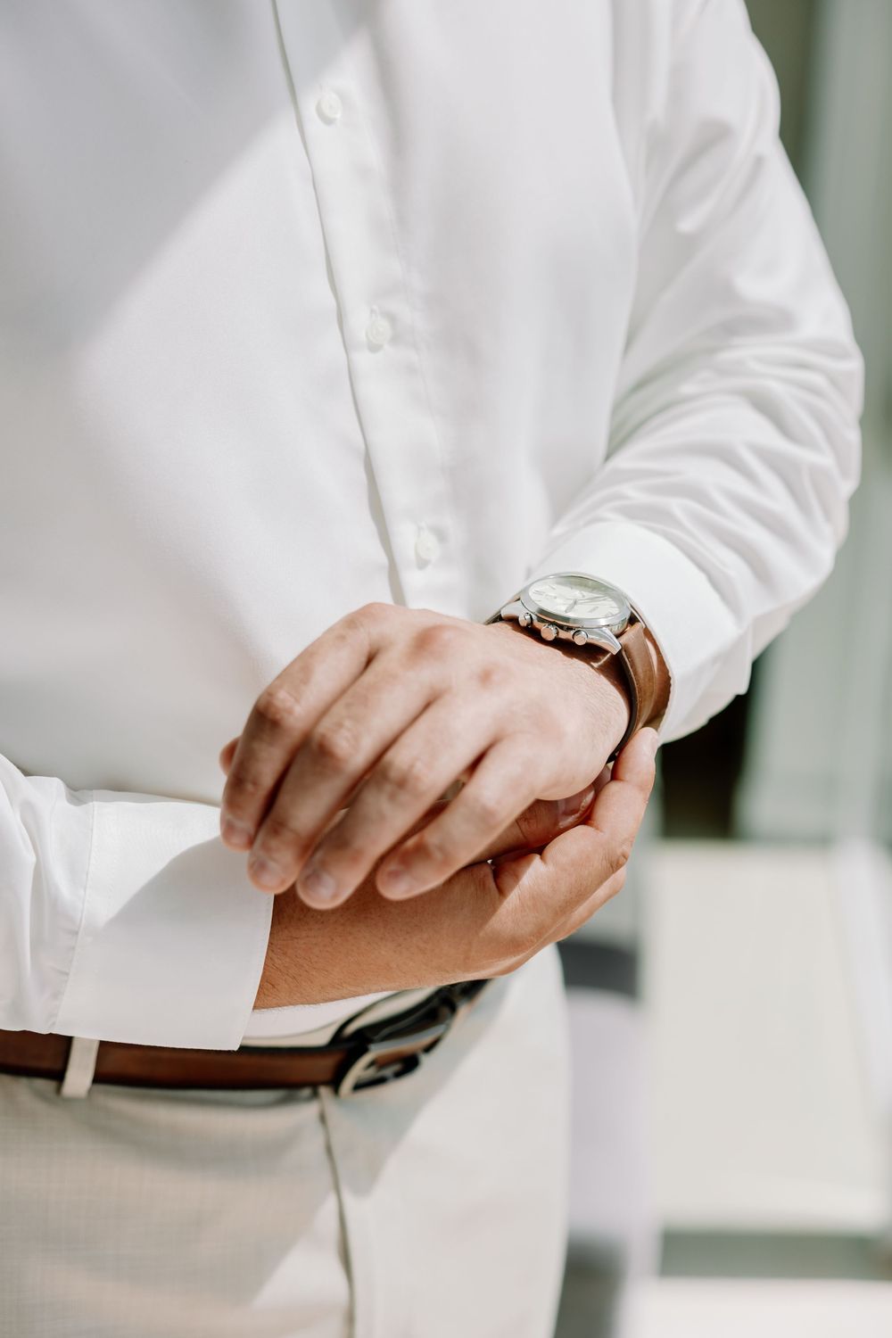 Close-up of hands adjusting elegant wristwatch against crisp white formal attire.