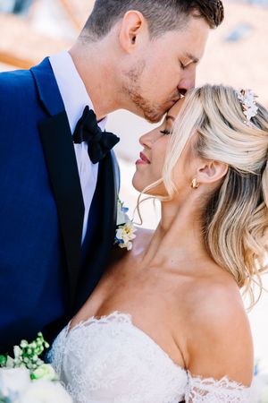 Romantic wedding couple shares intimate close-up moments in elegant attire with white floral boutonniere.