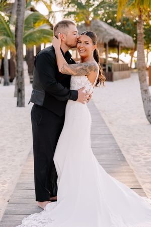 Newlyweds sharing intimate moment on tropical boardwalk surrounded by palm trees.