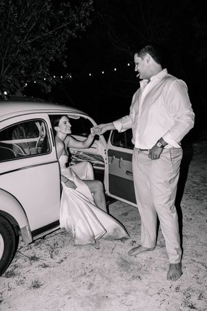 Vintage Volkswagen Beetle at night with couple in formal attire.