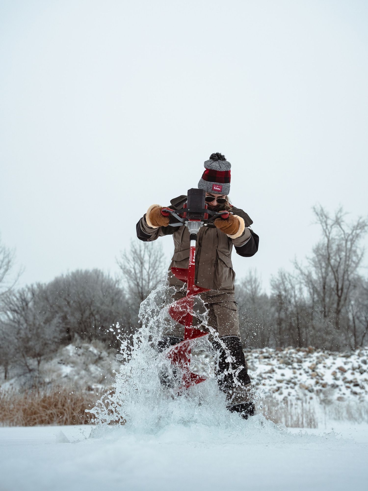 Action shot of ice fishing drill spraying snow while creating hole in frozen lake.
