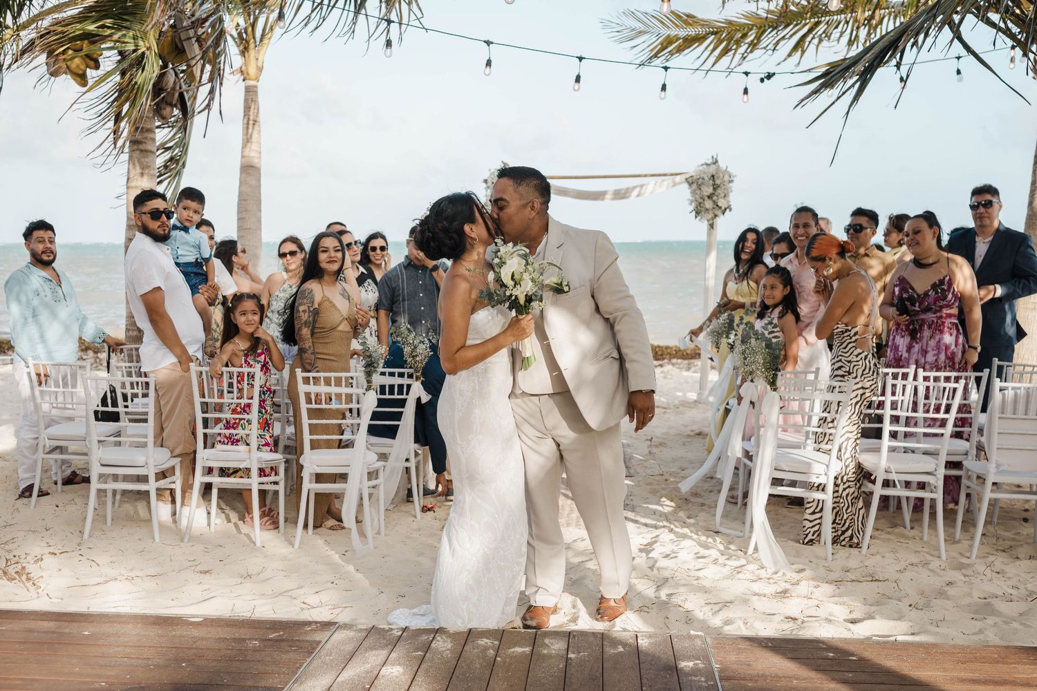 Outdoor beach wedding ceremony setup with white chairs and tropical decor against ocean backdrop, Casa Lu Puerto Morelos.