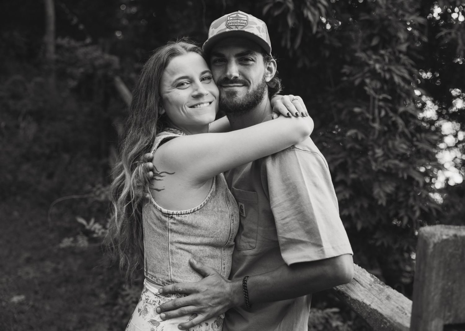 A couple embraces and laughs together while taking black and white photos outdoors in a natural setting.