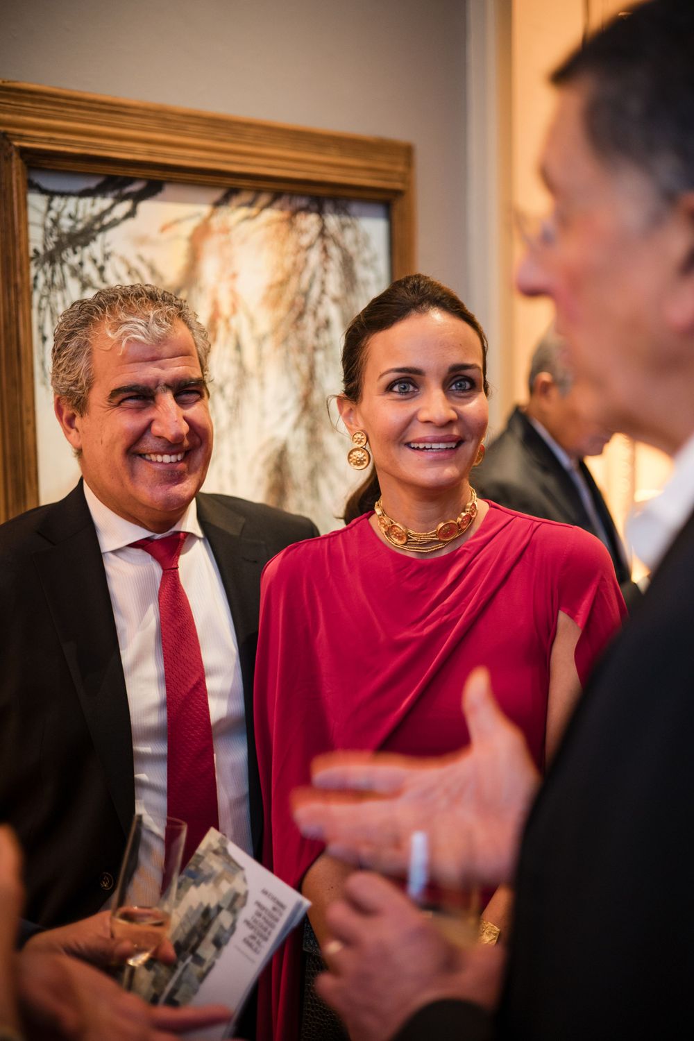 Guests in formal attire share a lighthearted moment at an elegant indoor gathering.