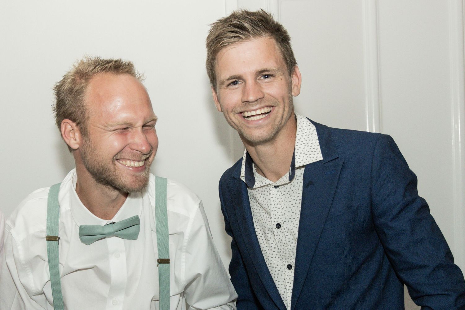 Two stylishly dressed companions sharing a cheerful moment indoors at an event.