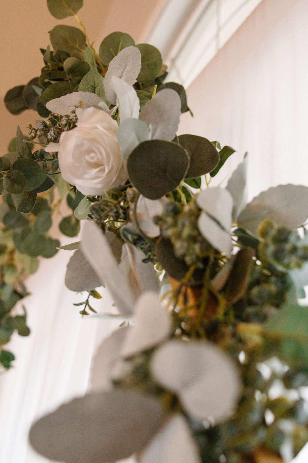 Elegant floral arrangement with white roses and eucalyptus leaves against a light wall.