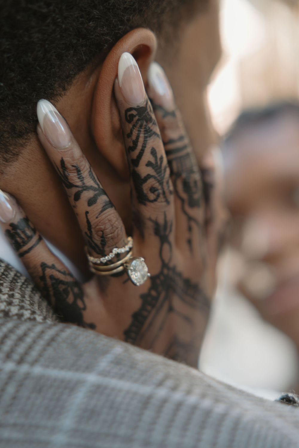 Close-up of tattooed hand with engagement ring against plaid suit fabric.