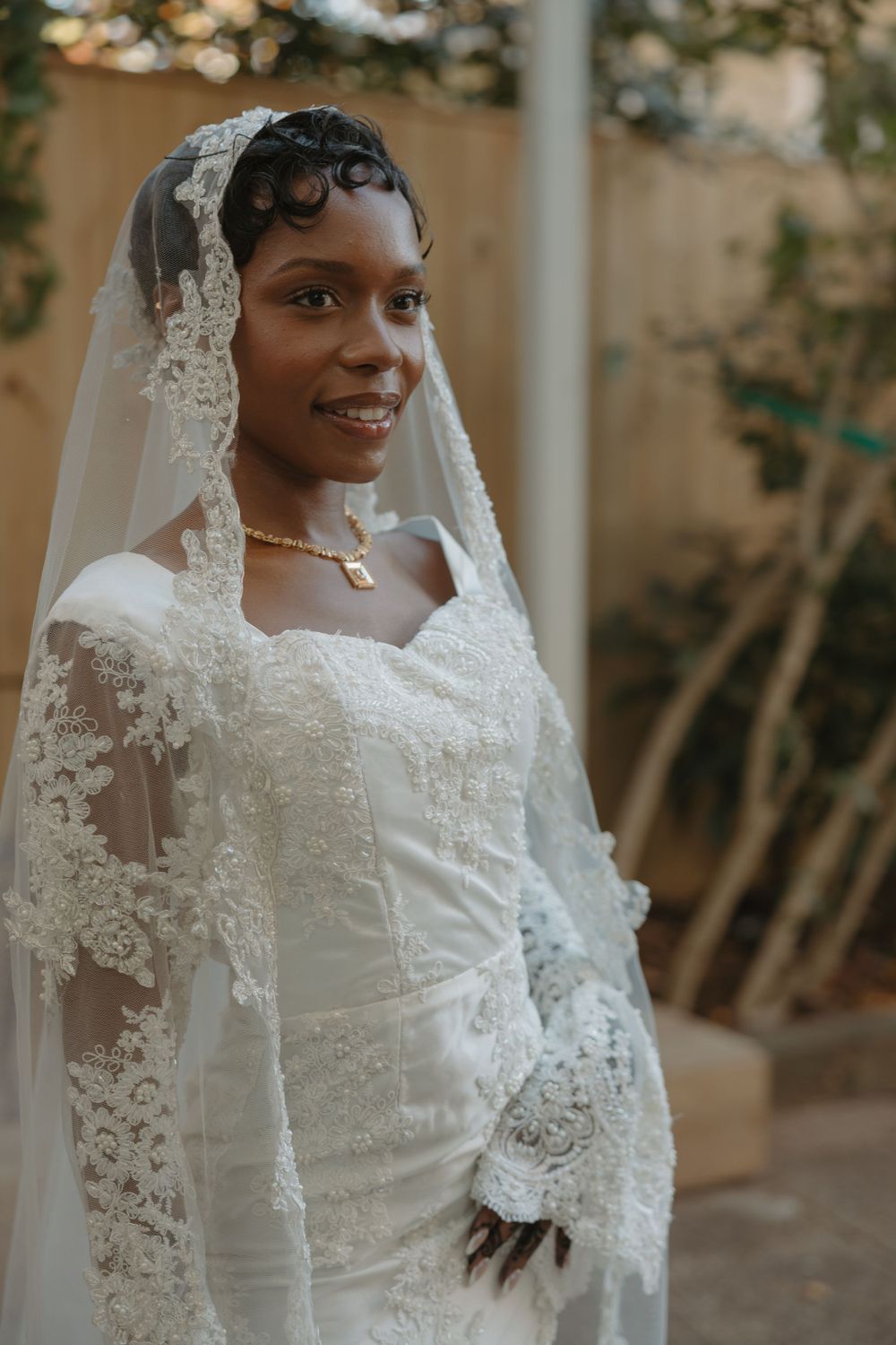 Radiant bride poses in an exquisite white lace wedding gown with cathedral veil against natural backdrop.