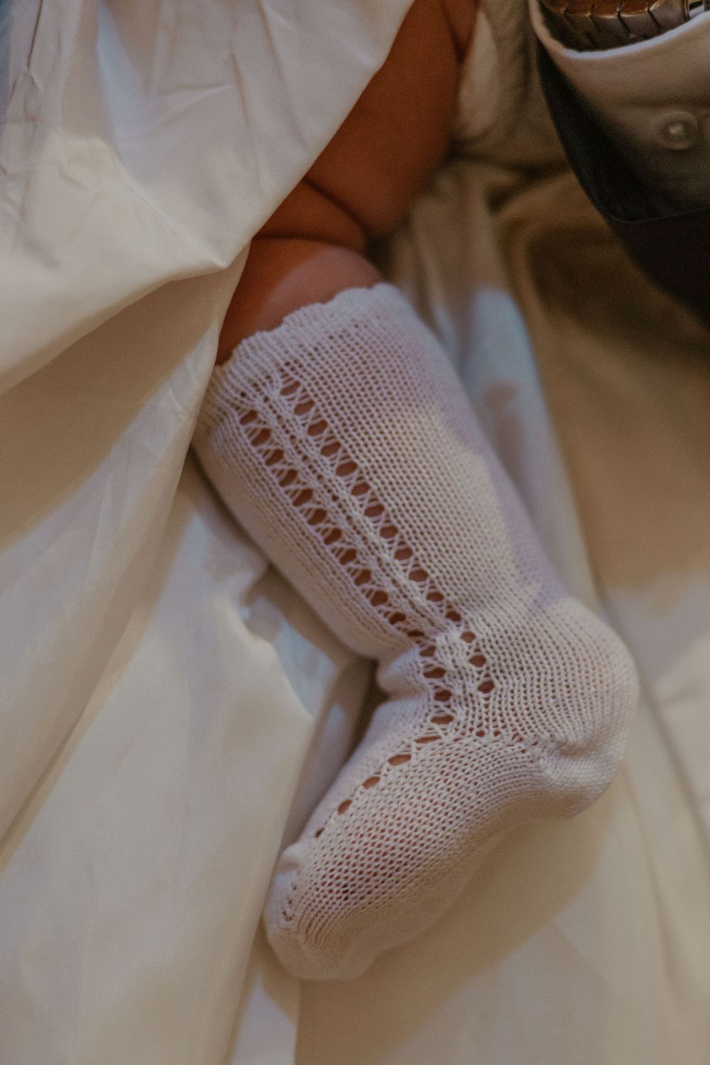 Close-up of delicate white knit christening sock with intricate lace pattern detail.