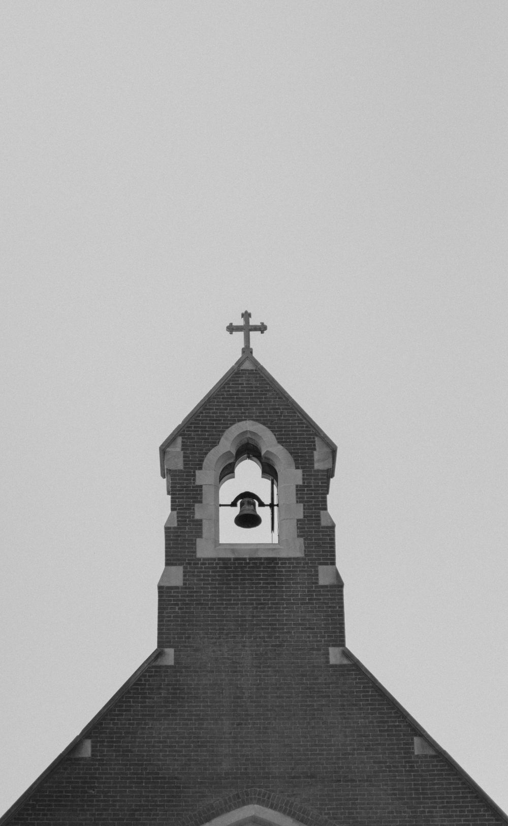 Minimalist black and white view of church bell tower with cross against grey sky.