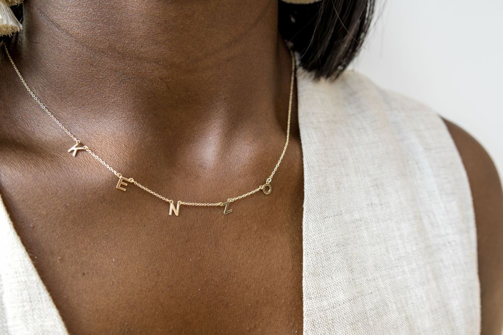 Close-up of a delicate letter necklace worn against dark skin.