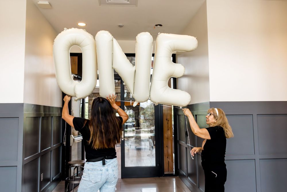 People installing large white balloon letters spelling 'ONE' on a grey wall.