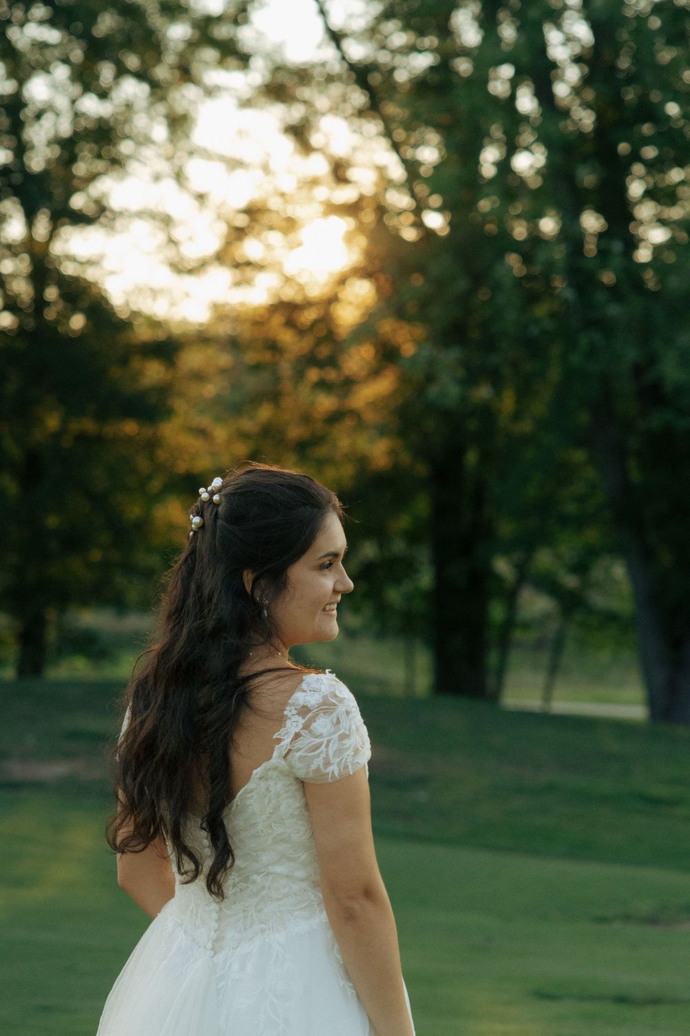A romantic sunset view captures a bride in a white gown with flowing dark hair and lace details.