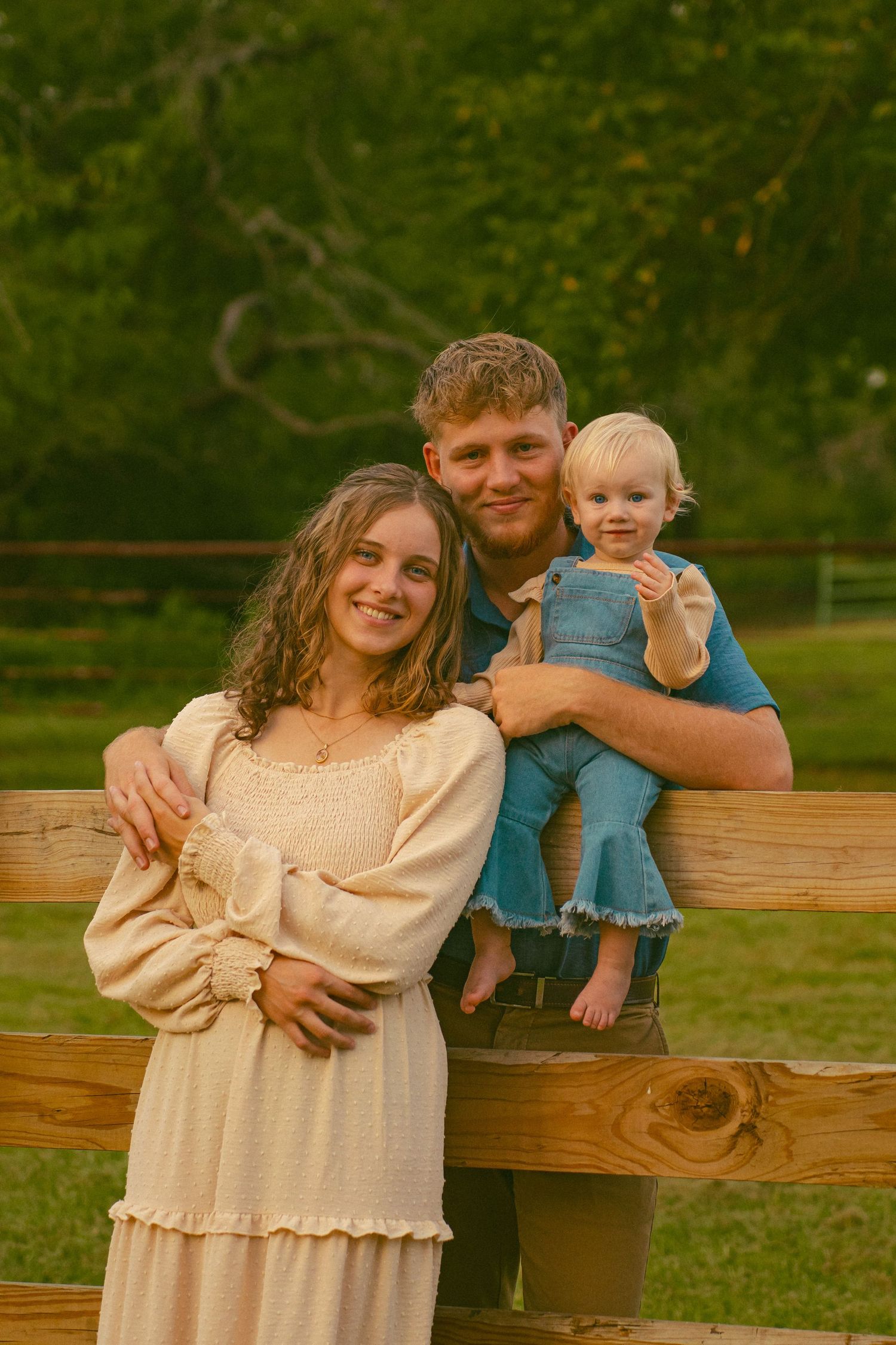 Family posing together on wooden fence in park during sunset.