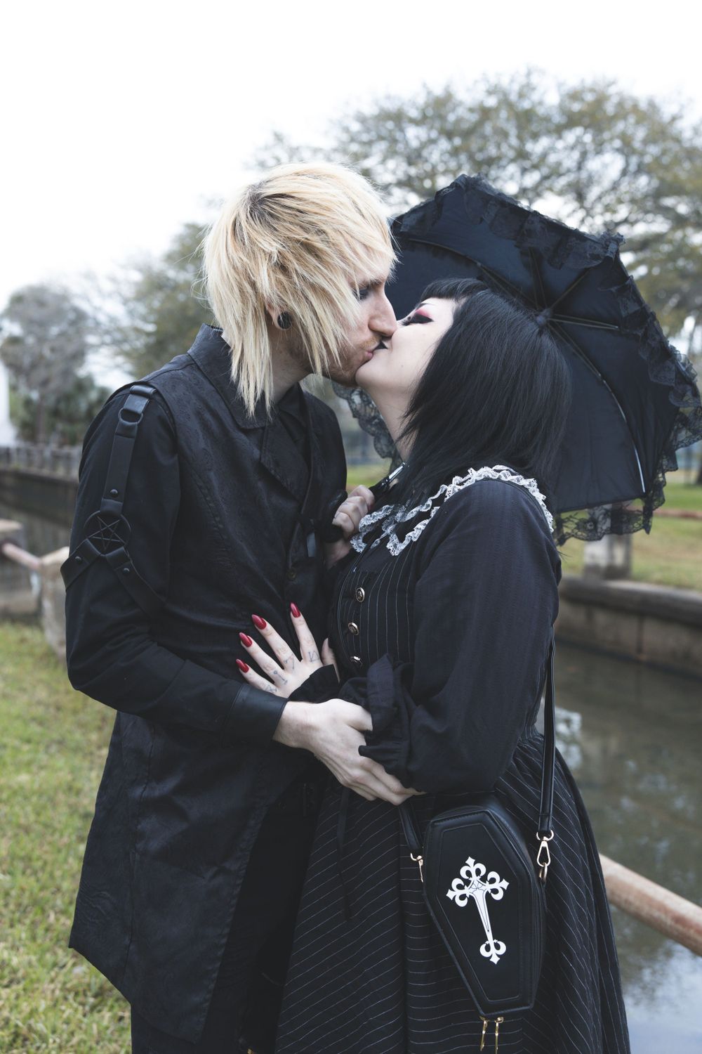 Romantic gothic couple in black attire sharing intimate moment by historic waterway.