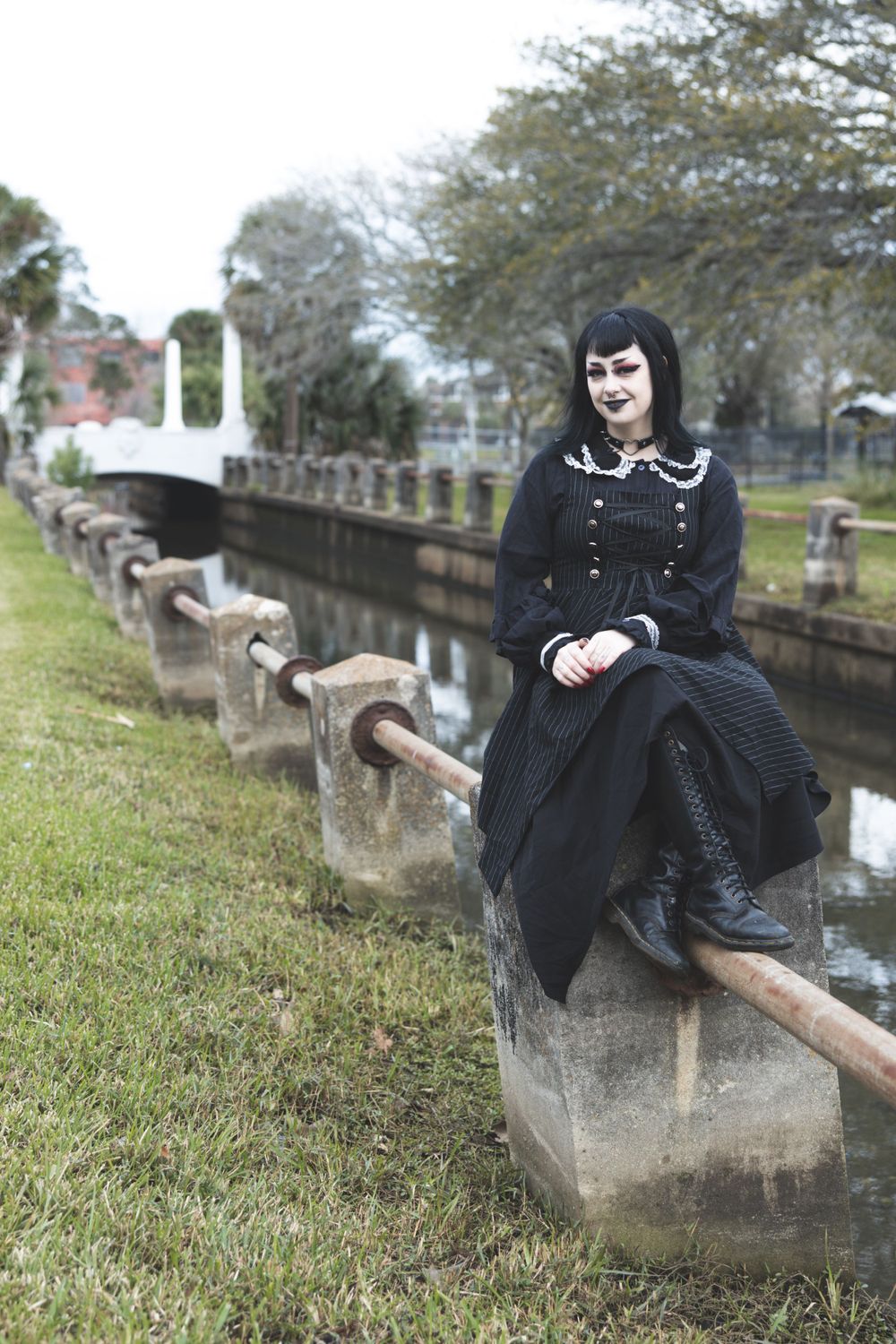 Gothic fashion photo of person in black dress posed along historic canal railing.