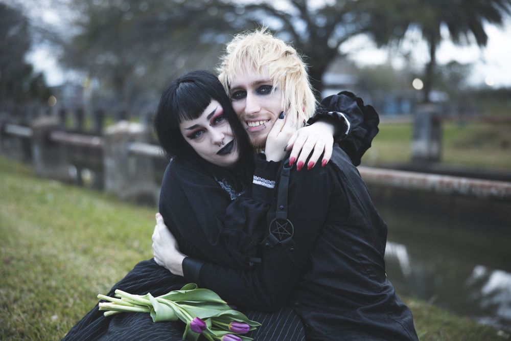 Alternative style couple in dark clothing sharing playful moment by water.