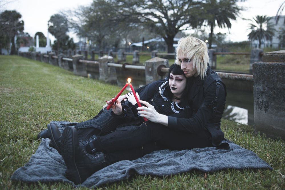 Gothic couple relaxing on blanket in cemetery sharing intimate moment.