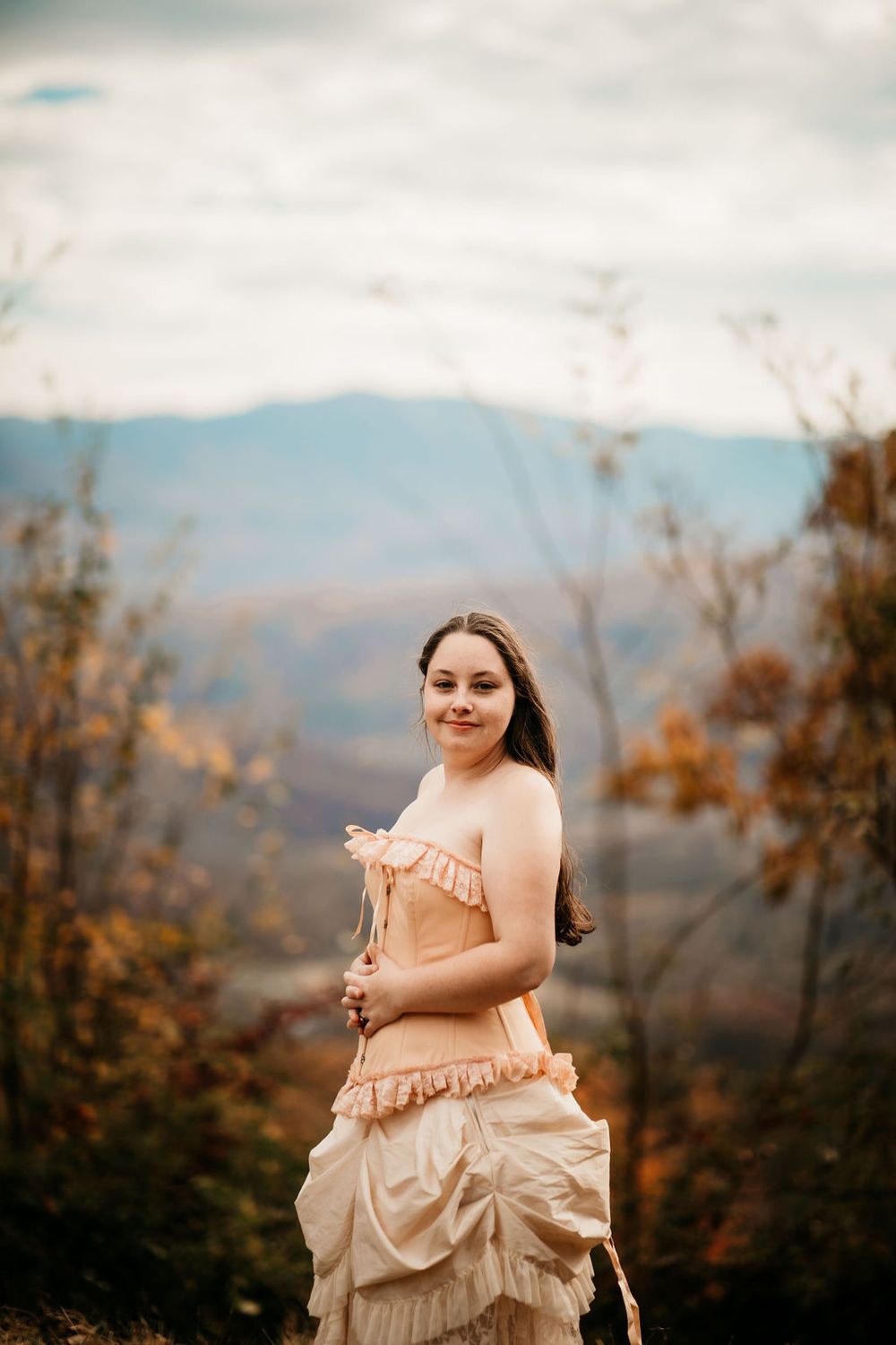 Person in vintage-style ruffled dress poses against mountain landscape at sunset.