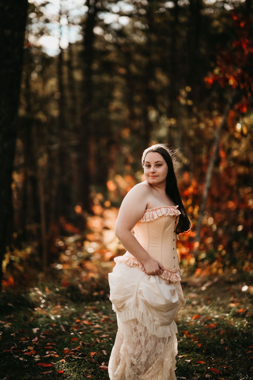Elegant vintage-style photoshoot in autumn forest with warm lighting and fallen leaves.
