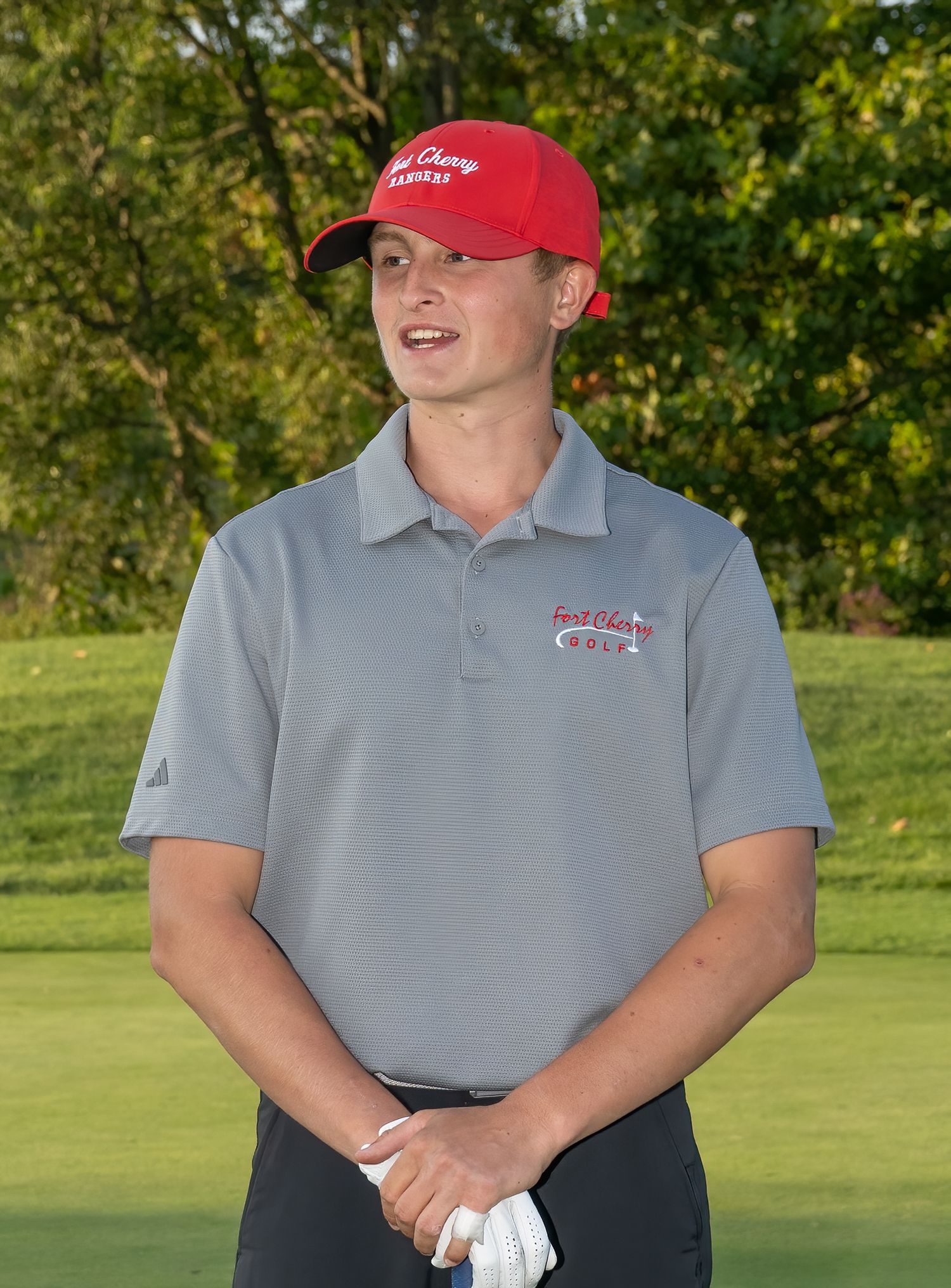 Golfer in gray polo shirt and red cap standing on golf course.