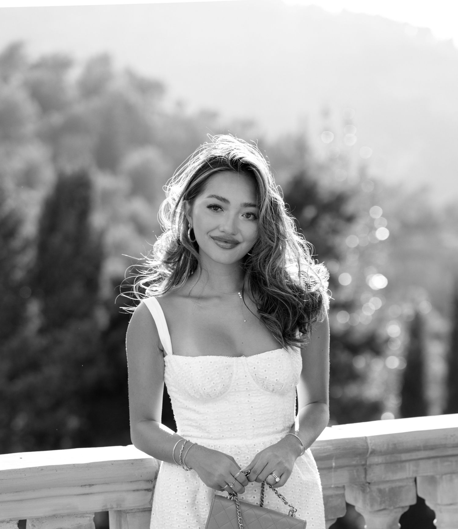 A woman in a white summer dress poses on a balcony in black and white photography.