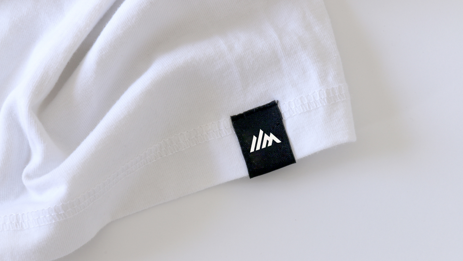 Close-up of a white fabric tag with a minimalist mountain logo design.