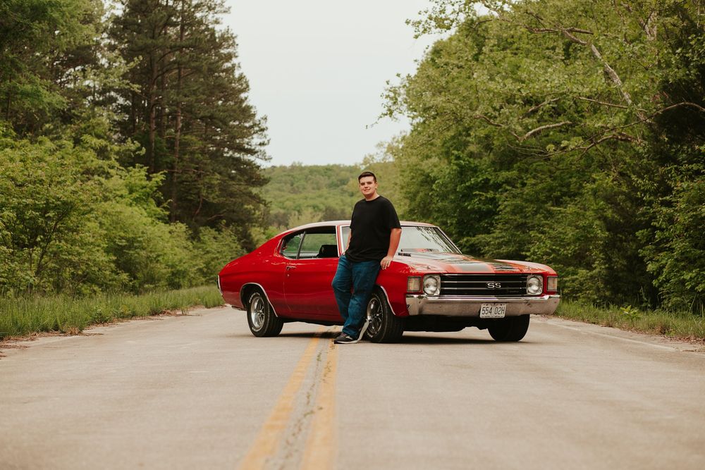 boy posing with a red chevelle car