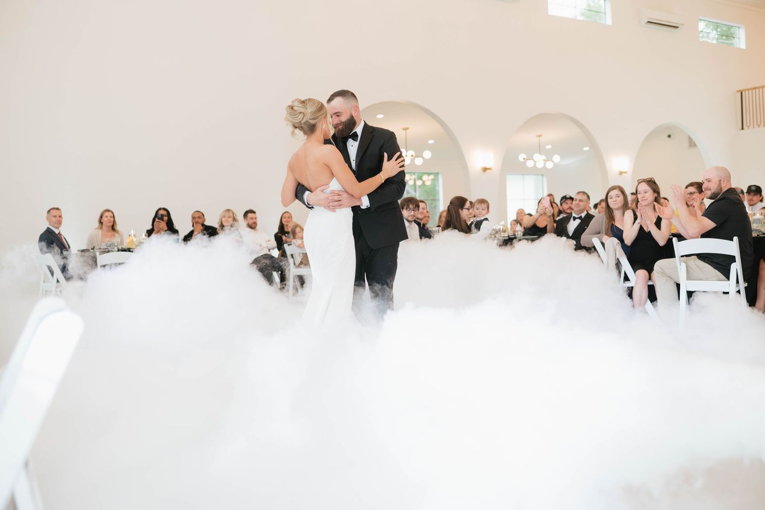 Newlyweds embrace in mountain meadow with dramatic landscape backdrop.
