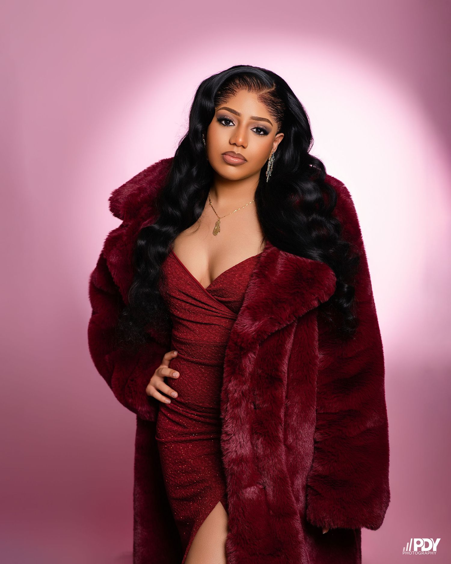 Stylish portrait showcasing burgundy fur coat and matching dress with dramatic lighting.