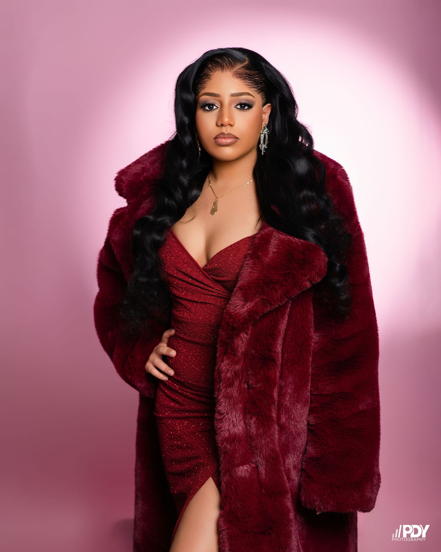 Glamorous portrait featuring deep red fur coat and sparkly dress with side slit.